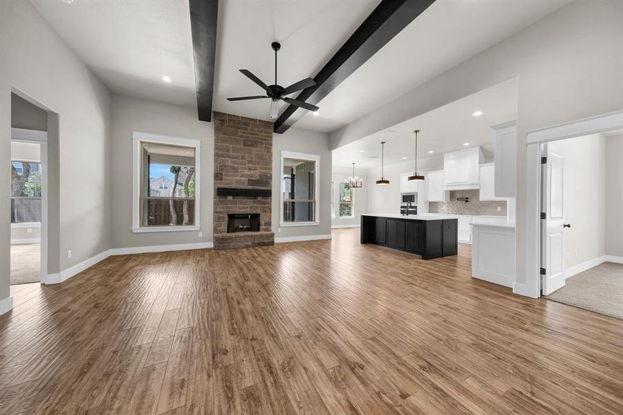 Unfurnished living room with beamed ceiling, ceiling fan, a fireplace, and light wood-type flooring