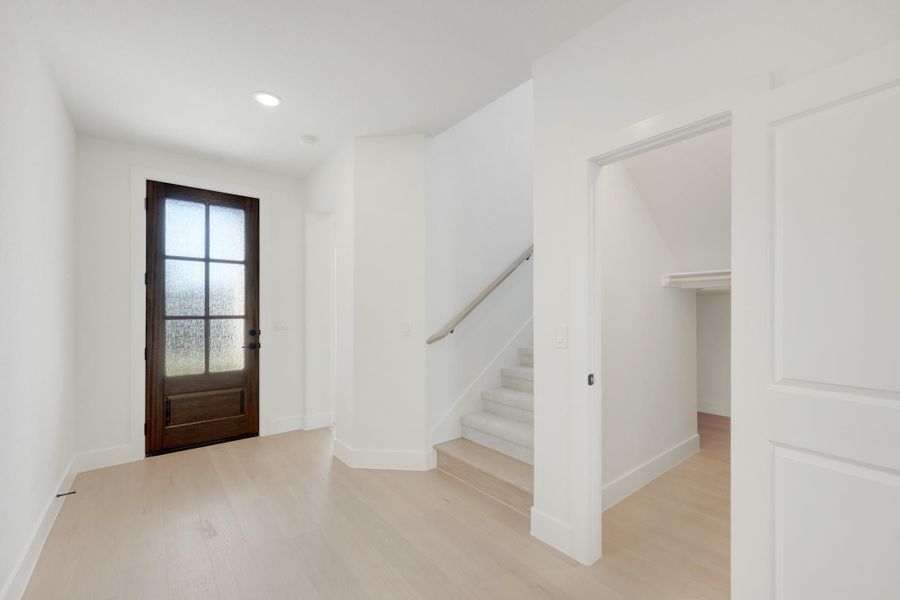 Entryway with dark wood glass-panel front door, staircase, and light hardwood floors in white walls