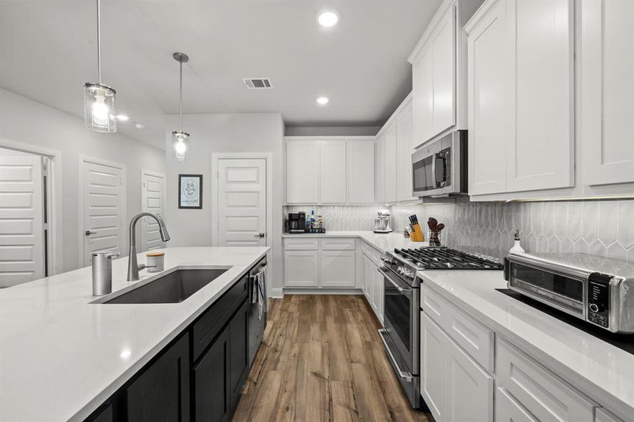 Kitchen with white cabinetry, decorative backsplash, appliances with stainless steel finishes, dark cabinets, and hanging light fixtures Kitchen with white cabinetry, decorative backsplash, appliances with stainless steel finishes, dark cabinets, and hanging light fixtures