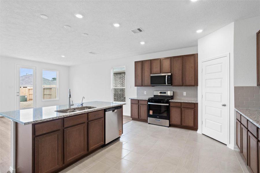 This spacious kitchen boasts soaring ceilings, Woodmont Cody cabinets in a Ginger stain, Granite Luna Pearl countertops, stainless steel Whirlpool appliances, a modern Daltile backsplash, recessed lighting, and a pantry—all overlooking the e This spacious kitchen boasts soaring ceilings, Woodmont Cody cabinets in a Ginger stain, Granite Luna Pearl countertops, stainless steel Whirlpool appliances, a modern Daltile backsplash, recessed lighting, and a pantry—all overlooking the e