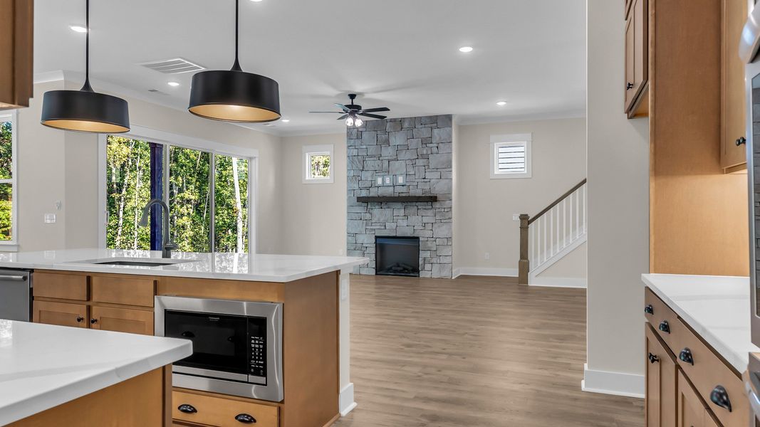 Kitchen with wood colored cabinetry and nearby gathering room (Representative of completed home)