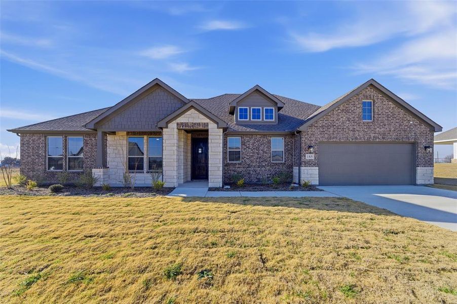 Craftsman-style house with a front lawn, concrete driveway, stone siding, and roof with shingles