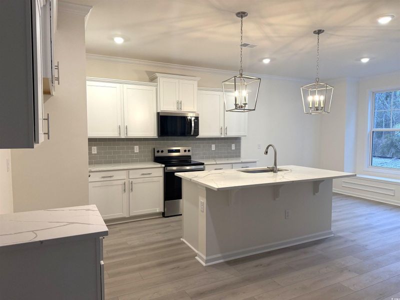 Kitchen featuring tasteful backsplash, quartz  countertops, white cabinetry, a kitchen breakfast bar, and crown molding