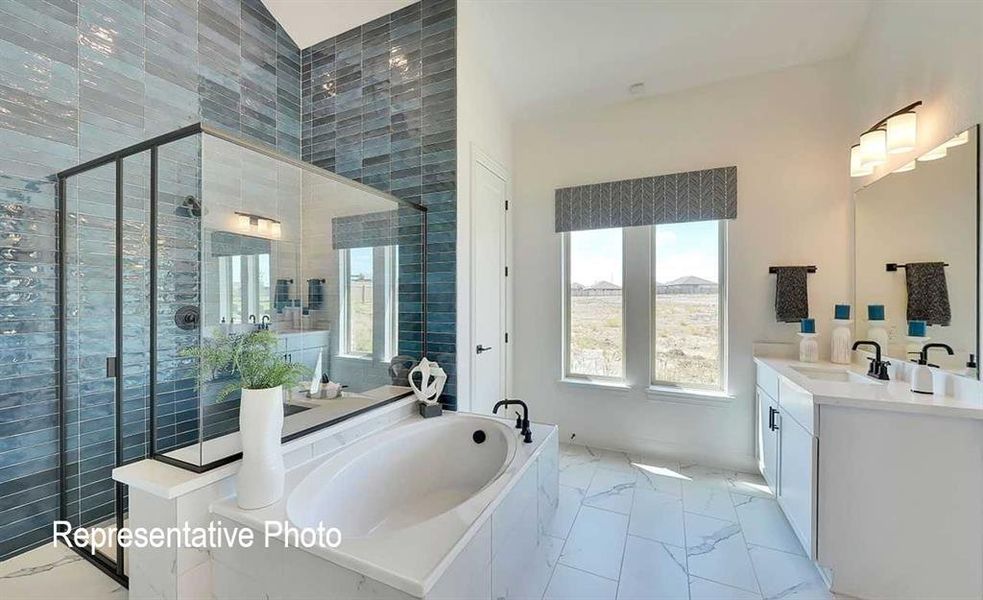 Contemporary bathroom featuring a spacious soaking tub, a separate glass-enclosed shower with blue-toned subway tile, dual vanities with white cabinetry, and large format marble-look floor tiles