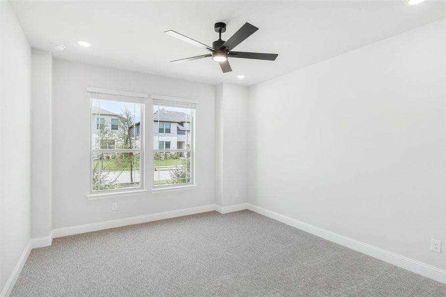 Empty bedroom with gray carpet, black ceiling fan, and two windows with neighborhood view