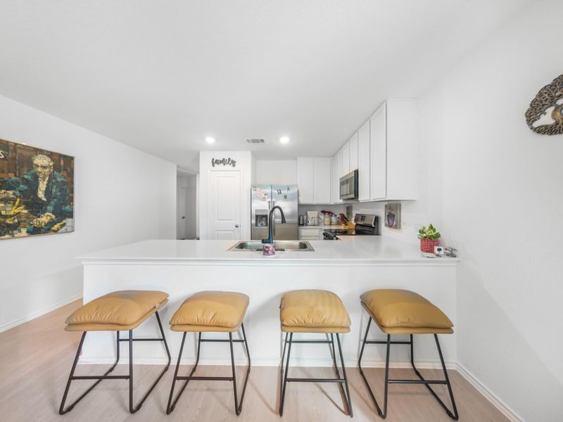 Kitchen with a kitchen bar, a peninsula, light countertops, white cabinets, and stainless steel appliances