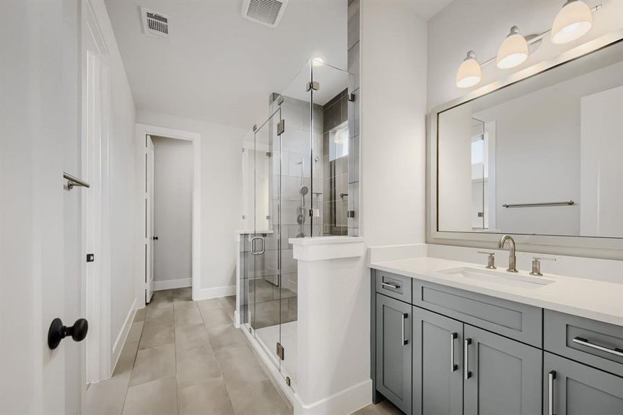 Modern bathroom featuring a frameless glass shower enclosure, a dual-sink vanity with light gray cabinetry, a rectangular wall-mounted mirror, and tile flooring