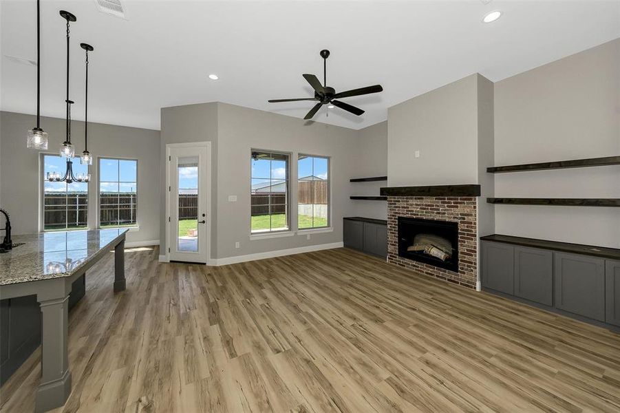 Unfurnished living room with a brick fireplace, ceiling fan, light wood-style flooring, recessed lighting, and a chandelier