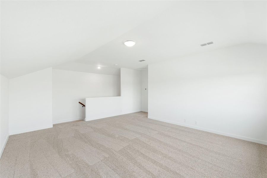 Open upstairs loft with vaulted ceiling, beige carpet, and staircase opening along white walls.