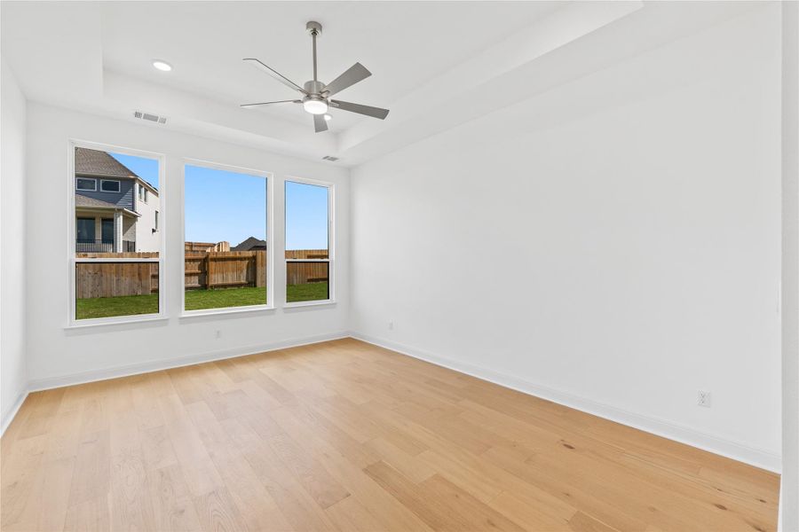Empty room with ceiling fan, a tray ceiling, and light wood-style floors