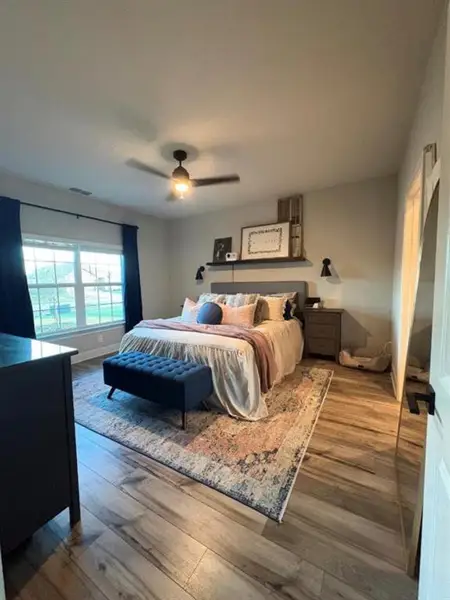 Spacious room featuring wood-finish flooring, a ceiling fan with integrated lighting, and substantial natural light from a large window
