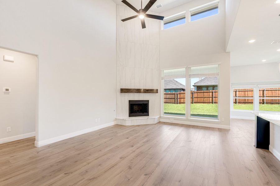 Open living room with two-story ceiling, tile fireplace, ceiling fan, and light hardwood floors Open living room with two-story ceiling, tile fireplace, ceiling fan, and light hardwood floors