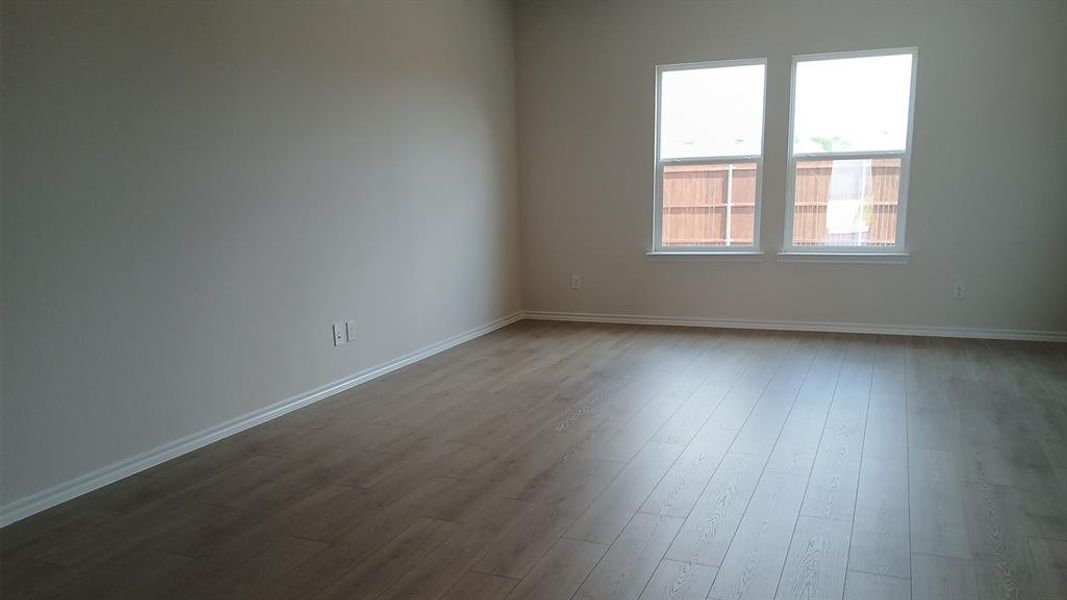 Expansive interior space featuring wood-finish flooring, two large windows, white baseboards, and neutral wall tones Expansive interior space featuring wood-finish flooring, two large windows, white baseboards, and neutral wall tones