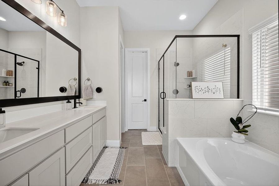 Bathroom featuring a dual vanity with light cabinetry and white countertops, a large framed mirror, a separate glass-enclosed shower with black trim, a built-in tub, and tile flooring