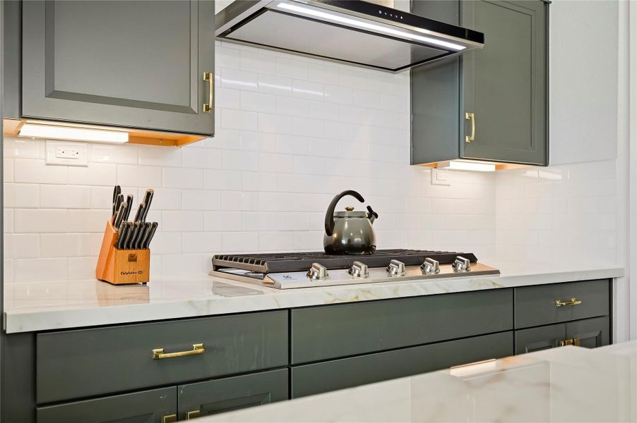 A five-burner gas cooktop is complemented by Quartz countertops and a classic subway tile back splash, creating a polished setting with generous space for preparing multiple dishes with ease. Gorgeous gold brushed hardware adds a decorative touch. A five-burner gas cooktop is complemented by Quartz countertops and a classic subway tile back splash, creating a polished setting with generous space for preparing multiple dishes with ease. Gorgeous gold brushed hardware adds a decorative touch.