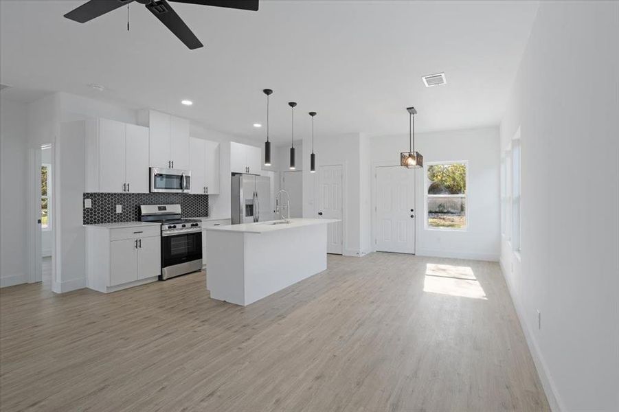 Kitchen featuring appliances with stainless steel finishes, pendant lighting, a center island with sink, light hardwood / wood-style flooring, and white cabinets