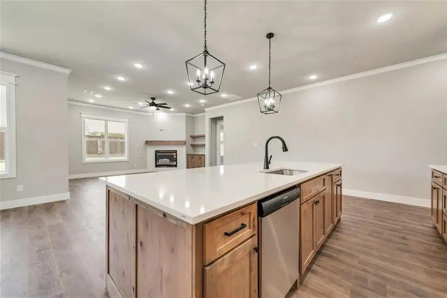 Kitchen with an island with sink, a fireplace, a ceiling fan, light wood finished floors, and dishwasher
