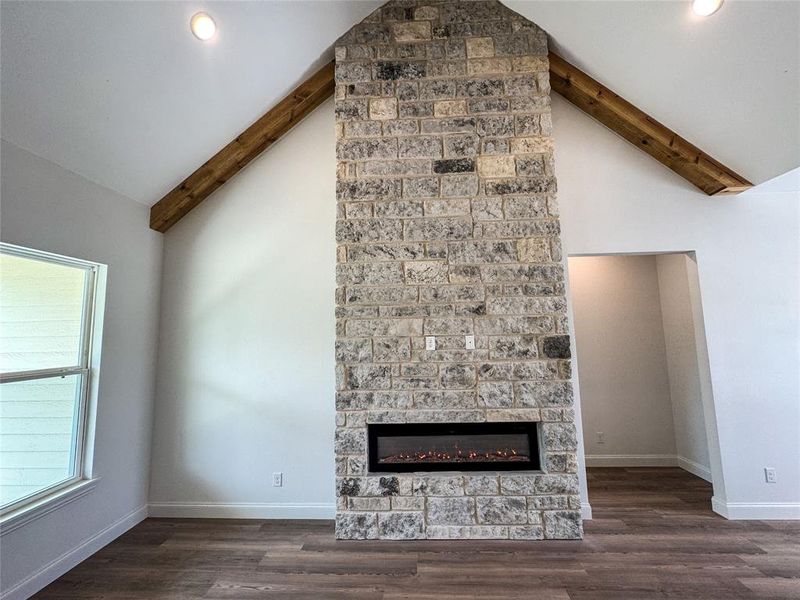 Unfurnished living room with beam ceiling, a stone fireplace, wood finished floors, baseboards, and recessed lighting Unfurnished living room with beam ceiling, a stone fireplace, wood finished floors, baseboards, and recessed lighting