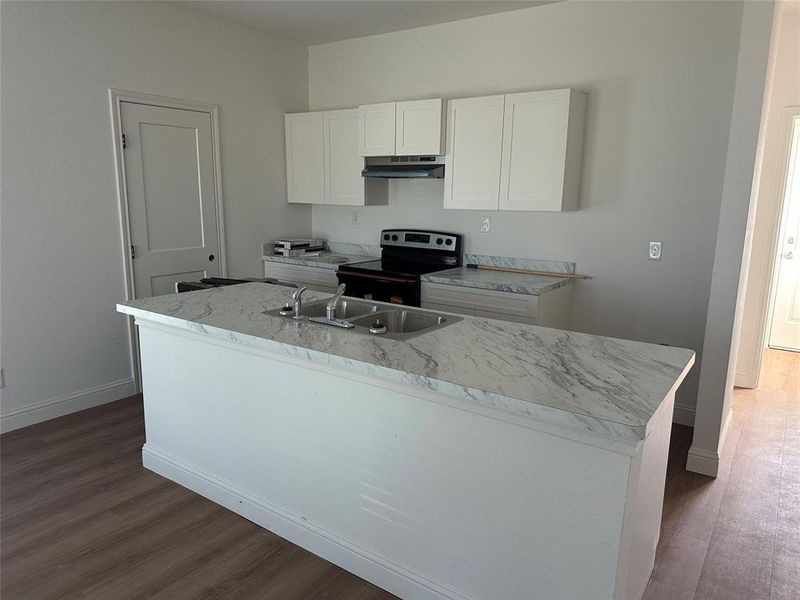 Kitchen with white cabinetry, stainless steel electric range oven, light countertops, dark wood-style floors, and an island with sink
