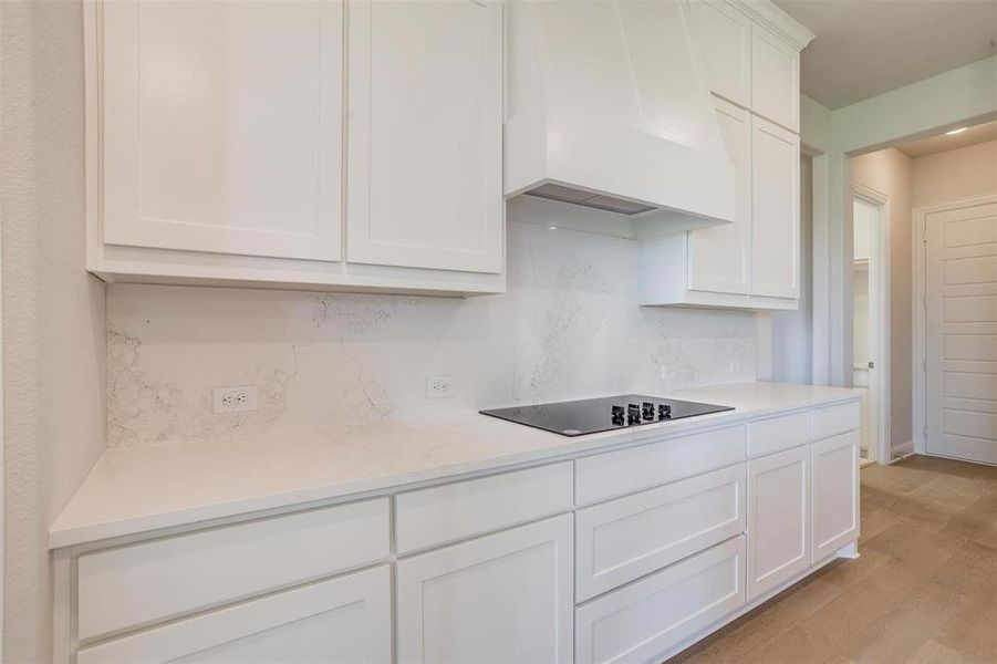 Kitchen with black electric cooktop, light hardwood / wood-style flooring, custom exhaust hood, light stone counters, and white cabinetry