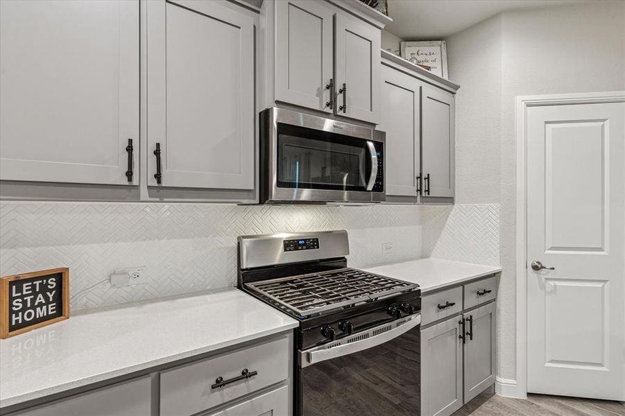 Kitchen featuring stainless steel appliances, gray cabinetry, tasteful backsplash, and light countertops Kitchen featuring stainless steel appliances, gray cabinetry, tasteful backsplash, and light countertops