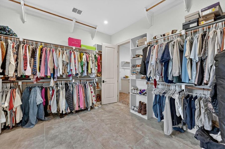 Expansive walk-in closet featuring large format floor tiling, white walls, recessed lighting, and extensive built-in storage