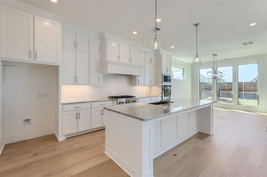 Kitchen featuring decorative light fixtures, a kitchen island with sink, sink, and white cabinetry