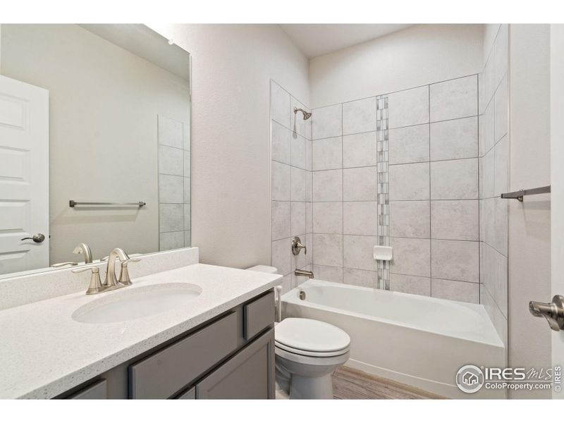 Hall bath with quartz counters and tiled shower