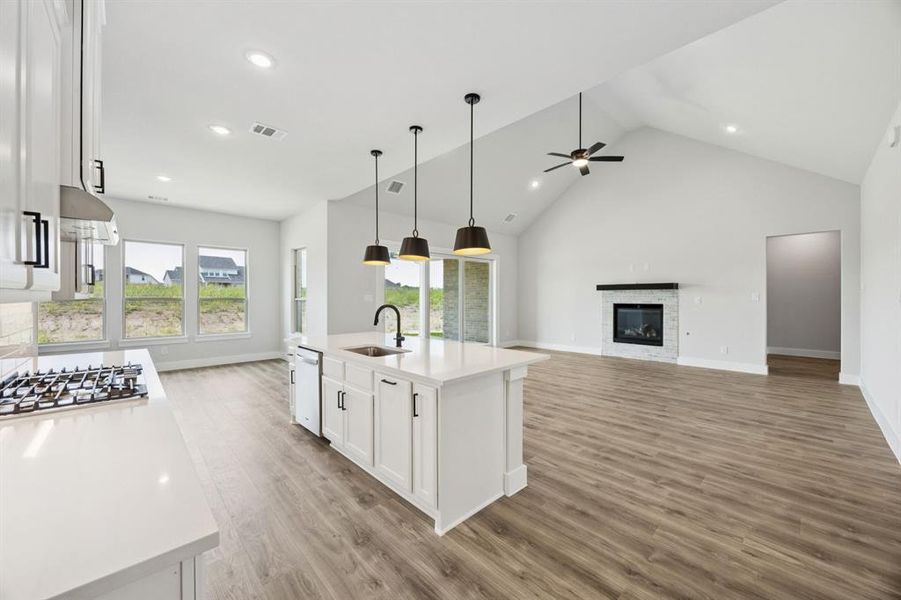 Kitchen with white cabinets, high vaulted ceiling, an island with sink, a glass covered fireplace, and open floor plan