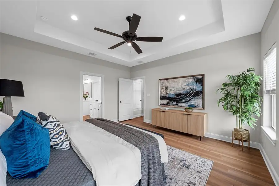 Bedroom featuring wood finished floors, a tray ceiling, a ceiling fan, recessed lighting, and ensuite bath Bedroom featuring wood finished floors, a tray ceiling, a ceiling fan, recessed lighting, and ensuite bath