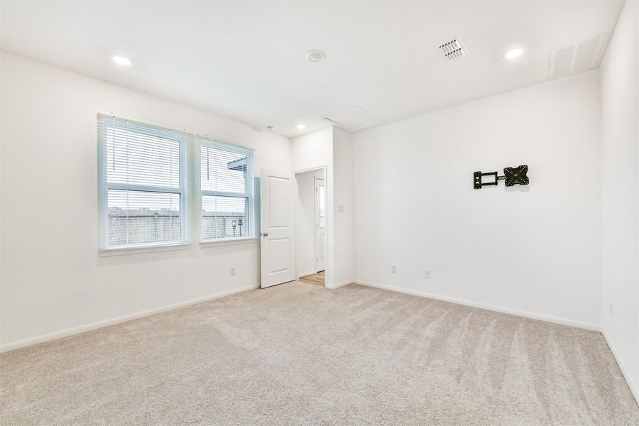 Another view of the primary bedroom located on the first floor. Plenty of natural lighting and lush carpet.