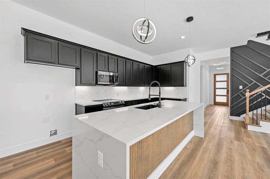 Kitchen with light hardwood / wood-style flooring, backsplash, appliances with stainless steel finishes, light stone countertops, and sink