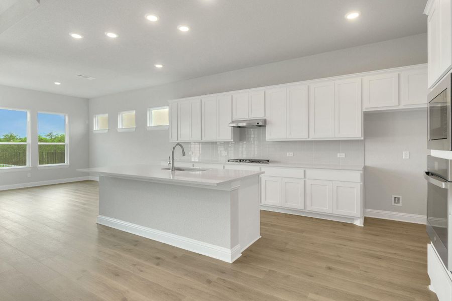 Kitchen featuring baseboards, under cabinet range hood, a sink, light wood-style flooring, and backsplash