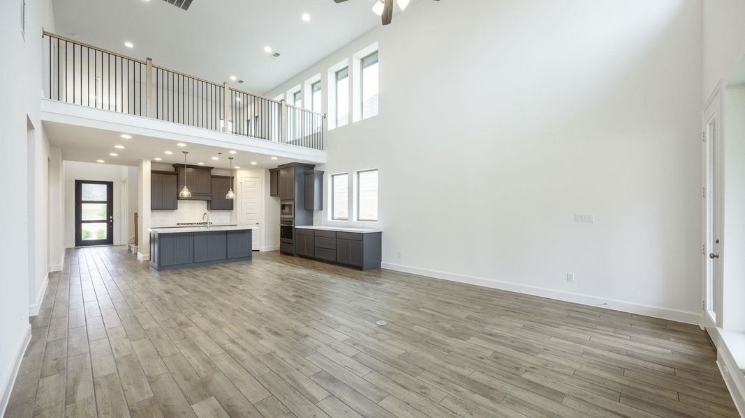 Unfurnished living room featuring light wood-type flooring, a ceiling fan, baseboards, and a towering ceiling Unfurnished living room featuring light wood-type flooring, a ceiling fan, baseboards, and a towering ceiling