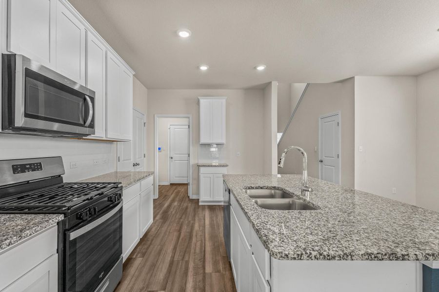 Kitchen featuring appliances with stainless steel finishes, dark wood-type flooring, white cabinetry, recessed lighting, and light stone countertops Kitchen featuring appliances with stainless steel finishes, dark wood-type flooring, white cabinetry, recessed lighting, and light stone countertops