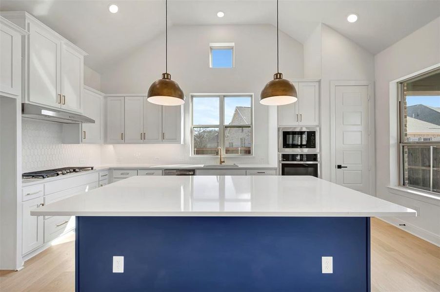 Kitchen with a kitchen island, stainless steel appliances, dual tone cabinetry, decorative light fixtures, and light wood-type flooring Kitchen with a kitchen island, stainless steel appliances, dual tone cabinetry, decorative light fixtures, and light wood-type flooring