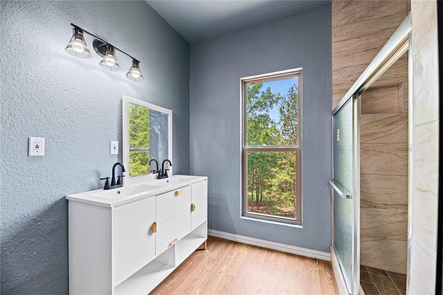 Bathroom featuring a shower with shower door, dual bowl vanity, and hardwood / wood-style floors Bathroom featuring a shower with shower door, dual bowl vanity, and hardwood / wood-style floors