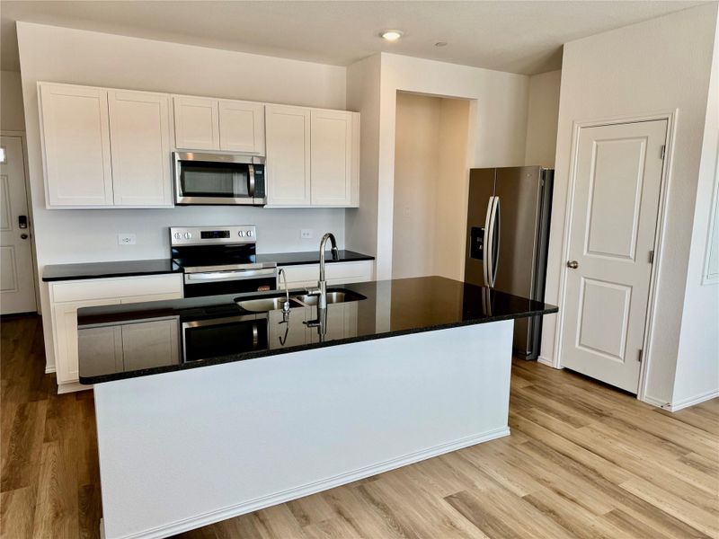 Kitchen featuring white cabinets, stainless steel appliances, light wood-style flooring, dark stone counters, and a kitchen island with sink