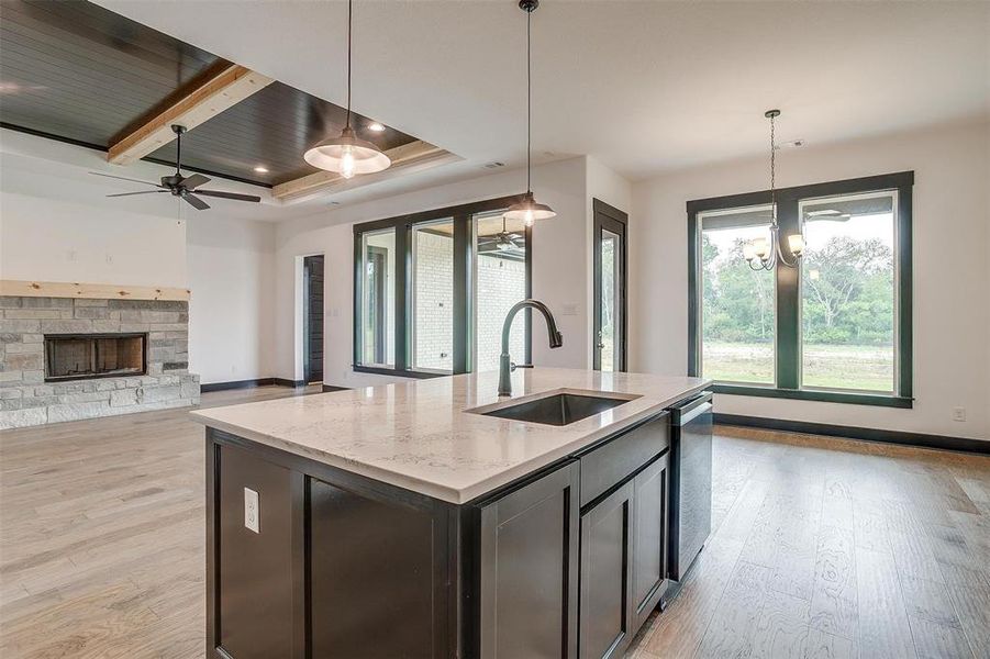 Kitchen with a tray ceiling, a fireplace, light wood-type flooring, sink, and a kitchen island with sink