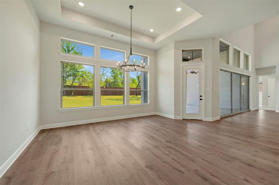 Unfurnished dining area with hanging lights, a high tray ceiling, and light wood-type flooring