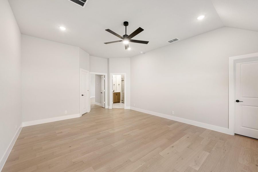 Empty bedroom with light hardwood floors, black ceiling fan, and open ensuite bathroom doorway Empty bedroom with light hardwood floors, black ceiling fan, and open ensuite bathroom doorway