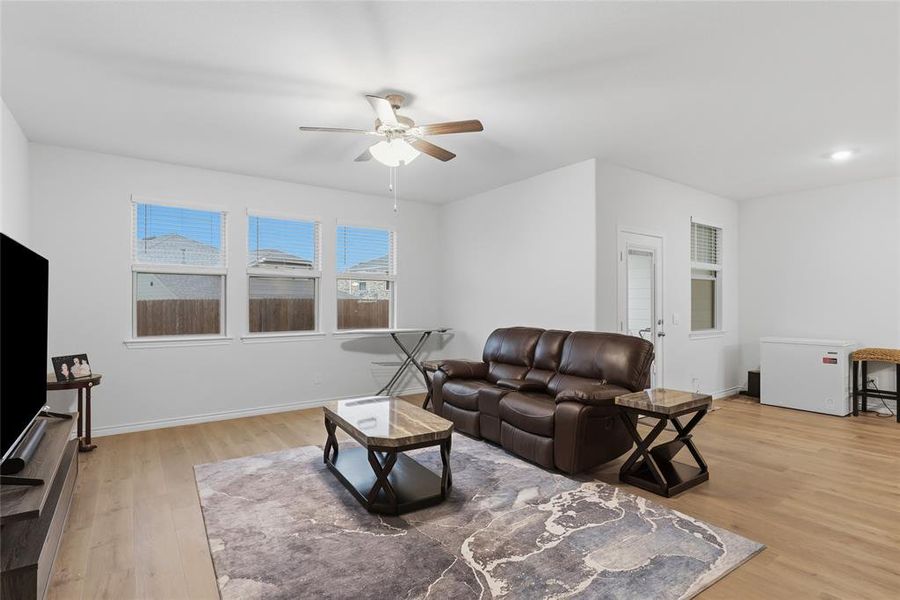 Open-concept living area featuring wood-finish flooring, white walls, and a ceiling fan with integrated lighting