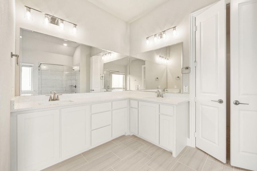 Bathroom with L-shaped white vanity, dual sinks, large mirrors, and a glass shower enclosure