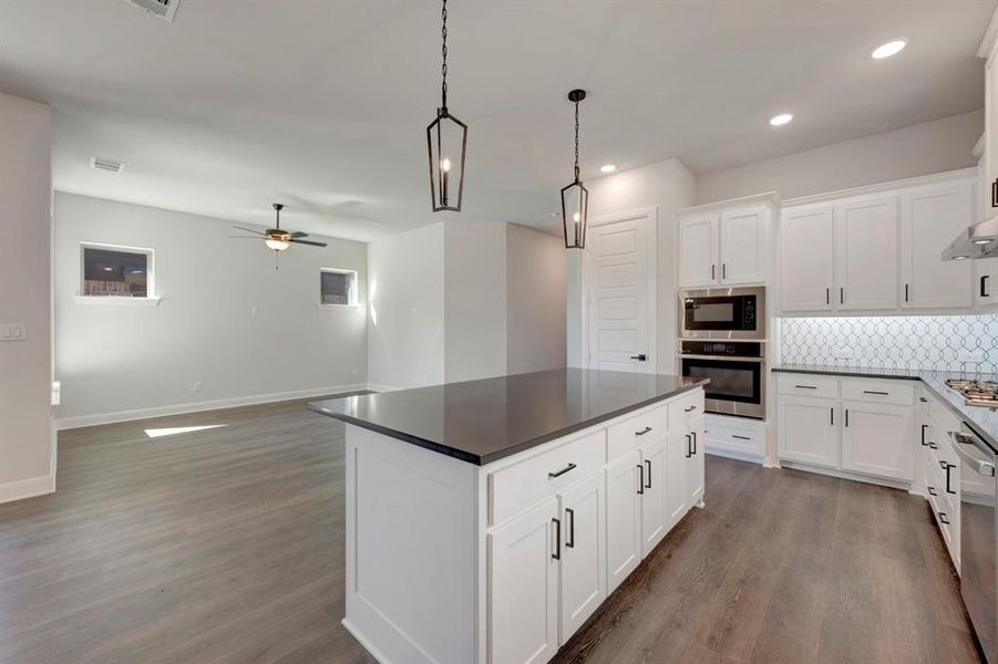 Kitchen with a kitchen island, white cabinets, tasteful backsplash, stainless steel appliances, and dark wood-style flooring