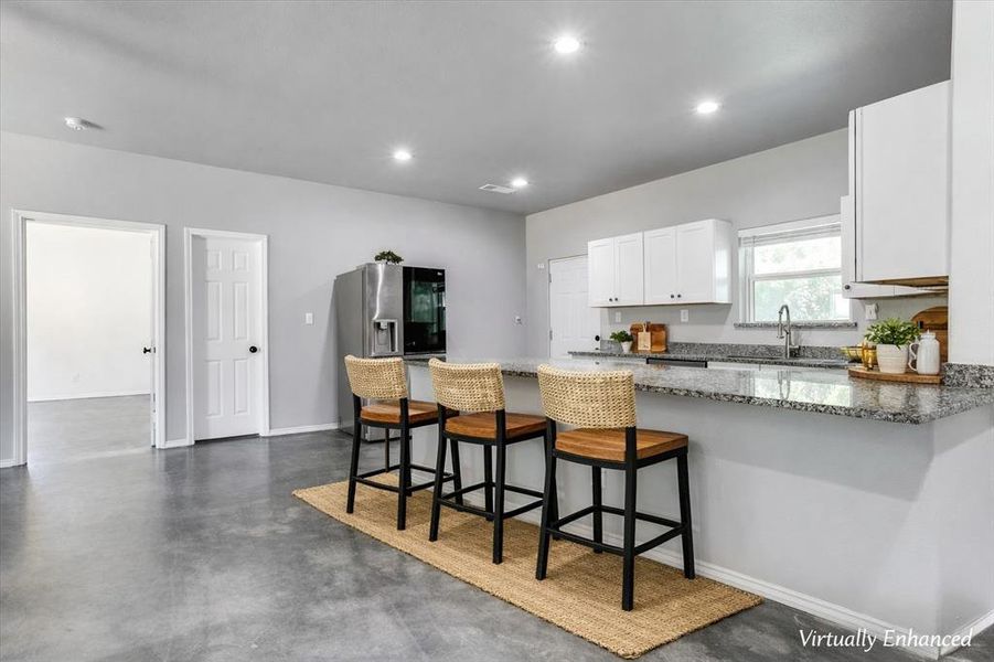 Kitchen featuring a breakfast bar with stone countertops, white shaker cabinetry, stainless steel appliances, a window above the sink, and recessed lighting