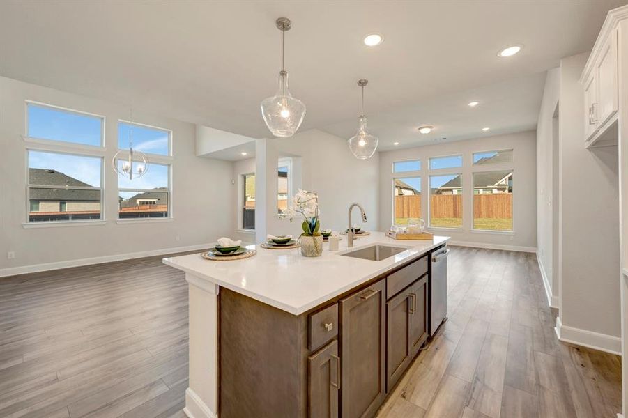 Kitchen featuring hanging light fixtures, light wood-type flooring, a center island with sink, and open floor plan