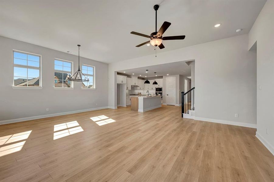 Unfurnished living room featuring light wood-style floors, ceiling fan, and suspended lighting