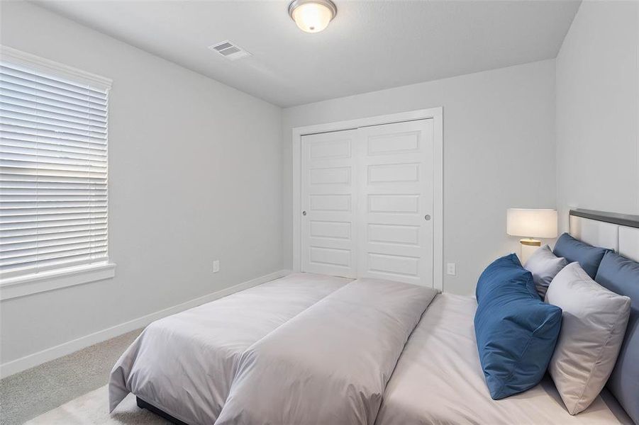 Secondary bedroom features plush carpet, neutral paint, lighting and a large window with privacy blinds.