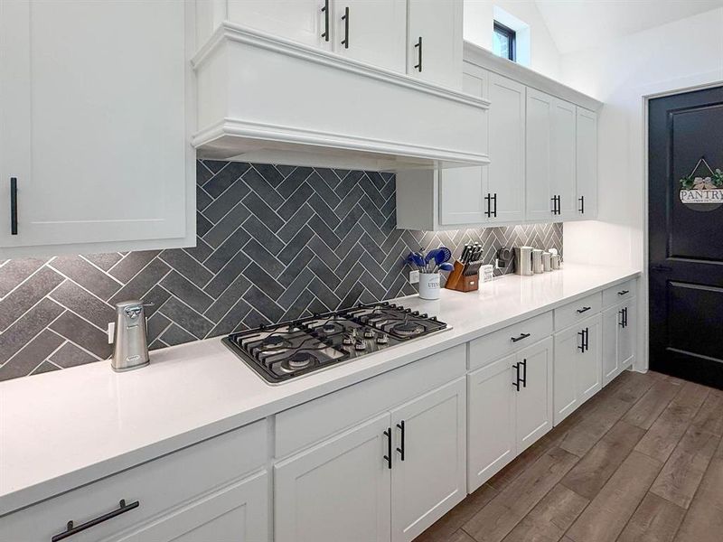 Kitchen with under cabinet range hood, white cabinets, backsplash, dark wood-style flooring, and stainless steel gas cooktop Kitchen with under cabinet range hood, white cabinets, backsplash, dark wood-style flooring, and stainless steel gas cooktop
