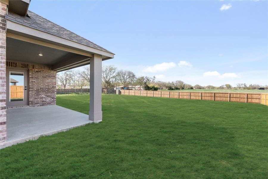 Large backyard with green lawn, covered patio, and wood privacy fence bordering open fields Large backyard with green lawn, covered patio, and wood privacy fence bordering open fields